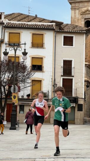 Två orienterare, en flicka i röd skjorta och en pojke i grön skjorta springer på gatorna jämsides.
